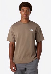 T-shirt marron à manches courtes en mélange de coton, avec un logo blanc sur le côté gauche de la poitrine, coupe décontractée et col rond.