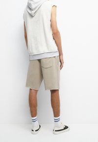 Hooded sleeveless fleece in off-white with gray accents, paired with beige shorts featuring a back pocket and raw hems. White socks and sneakers.
