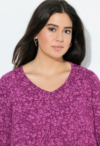 Blouse violette avec un motif floral, décolleté en V et des plis, fabriquée à partir d'un tissu léger au toucher doux.