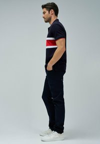 Námořnické polo tričko s červenými a bílými vodorovnými pruhy, v kombinaci s černými kalhotami a bílými sneakers, s klasickým střihem a krátkými rukávy.