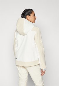 Hvid og beige hættejakke med en glat tekstur, der har kontrasterende paneler og en indpakket kant, velegnet til udendørs aktiviteter.