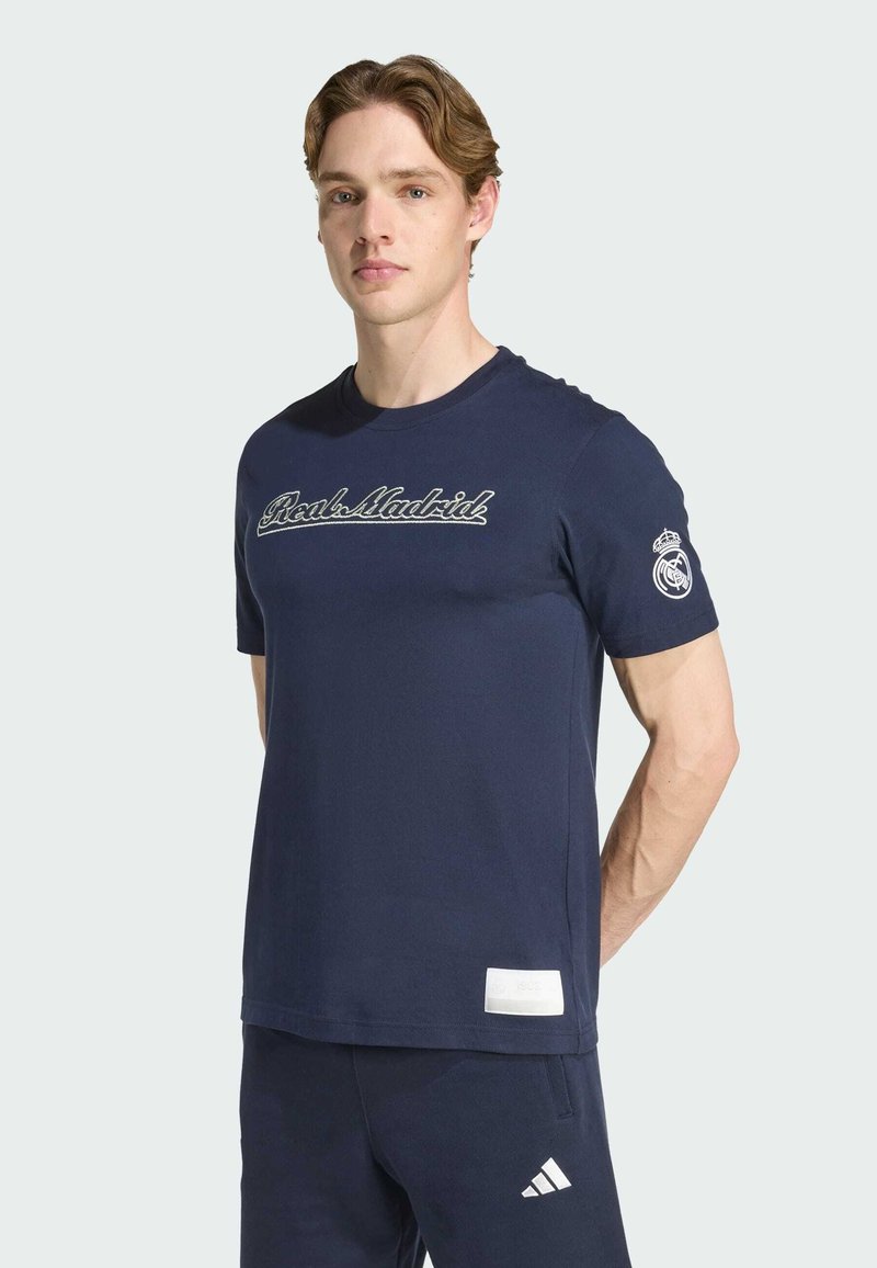 Camiseta de algodón azul marino con "Real Madrid" bordado en blanco, mangas cortas y un logo en la manga izquierda.