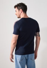 Camiseta de manga corta azul marino con acentos a rayas blancas y rojas en los hombros. Diseño ajustado, material de algodón, vista trasera lisa.