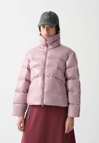 Vadderad jacka i glänsande ljusrosa material, med hög krage, framzipper och vida ärmar. Matchad med en mörkgrå keps.