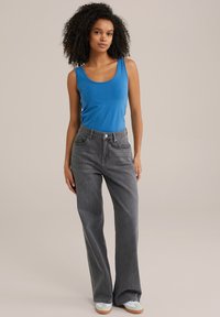 Modra brezrokavnik v kombinaciji z visokim pasom sivih širokih kavbojk. Teniske z svetlo zelenim zgornjim delom in bež podplatom. Gladke teksture tkanin.