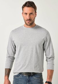 Pilkas ilgomis rankovėmis marškinėliai, pagaminti iš medvilnės mišinio, su apvalia iškirpte, šiek tiek prigludęs dizainas ir subtilus logotipas ant krūtinės.