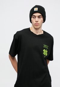 Czarna bawełniana koszulka z zielonym haftowanym motywem czterolistnej koniczyny oraz napisem "CARHARTT WIP POWODZENIA W DALSZEJ DRODZE".