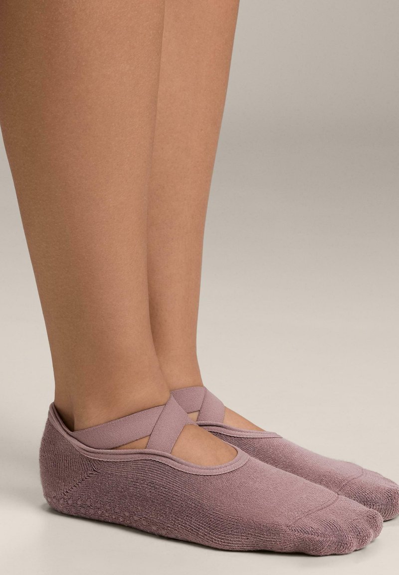 Ljuslila sockor med fotfäste och ett korsat remdesign vid anklarna, tillverkade av mjukt material och med en strukturerad yta.