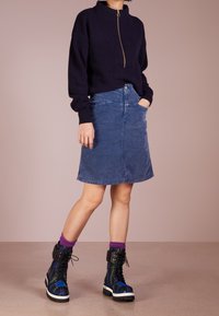 Marinefarbener Zip-Knit-Pullover, hellblauer Jeansrock, schwarze karierte Plateauboots mit lila Socken. Merkmale sind gerippte Bündchen und eine figurbetonte Silhouette.