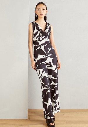 Combinaison sans manches en noir et blanc avec un motif floral, décolleté drapé, taille ceinturée et design à jambes larges. Portée avec des sandales à talons.