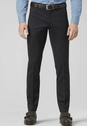 Homme portant un pantalon habillé noir coupe slim, une ceinture en cuir tressé marron et des chaussures à double boucle type monk strap tressées marron foncé.