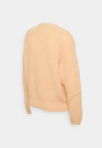 Ljusorange stickad tröja med avslappnad passform, rund halsringning och sänkta axlar. Strukturerad tyg med ribbad fåll och ärmslut.