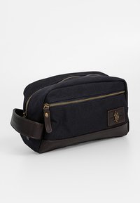 Laivastonsininen kangaslaukkku ruskeilla nahkasisustuksilla, kaksi vetoketjullista lokeroa ja sivukahva. Edessä on metallinen logopläkki.