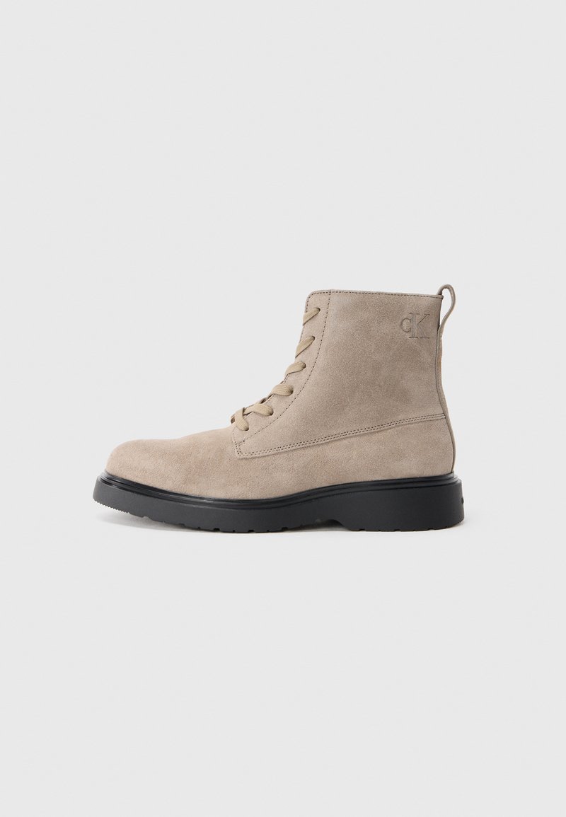 Stivaletti beige in suede con suola in gomma nera, design con lacci e piccolo logo impresso sul lato, dotati di un inserto sulla parte posteriore.