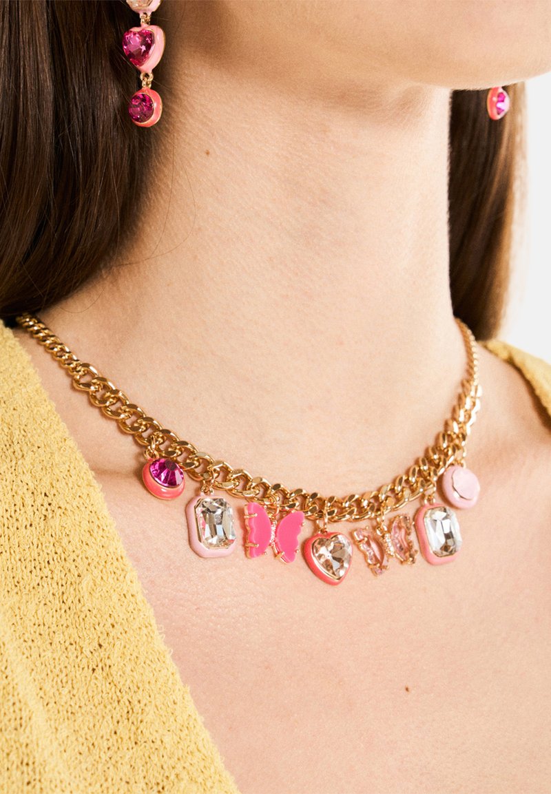 Collar de cadena dorada que presenta encantos decorativos en tonos rosa y claro, incluyendo mariposas y diversas formas, sobre un tejido claro y texturizado.