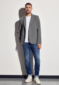 Harmaa pehmeä bleiseri valkoisen t-paidan päällä, yhdistettynä sinisiin farkkuihin ja valkoisiin lenkkareihin. Bleiserissä on laskostettu kaulus ja taskut.