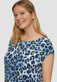 Blaues Kurzarmoberteil mit Leopardenmuster in Schwarz, Weiß und Gelb. Weiches Material und entspanntes Kragendesign.