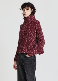 Kuscheliger roter Strickpullover mit hohem Kragen, strukturiertem Muster und überschnittenen Schultern, kombiniert mit dunklen, geraden Jeans.