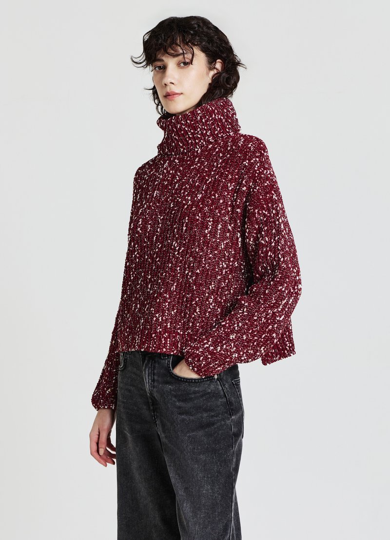 Kuscheliger roter Strickpullover mit hohem Kragen, strukturiertem Muster und überschnittenen Schultern, kombiniert mit dunklen, geraden Jeans.
