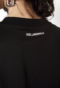 Czarna bawełniana koszulka z okrągłym dekoltem i haftowanym napisem "KARL LAGERFELD" na plecach, powyżej obszaru szyi.