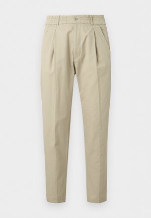Beige geplooide broek met knoopsluiting, riemlussen, zijzakken en taps toelopende pijpen, weergegeven tegen een witte achtergrond.