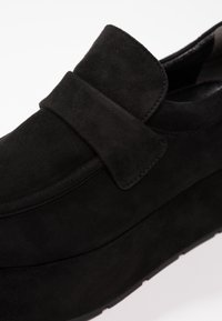 Mocassin à plateforme en daim noir avec une large bride sur le cou-de-pied et une semelle épaisse et texturée.