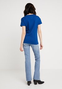 Blue cotton t-shirt with a regular fit, short sleeves, and a round neck, paired with light blue flared jeans and black heeled boots.