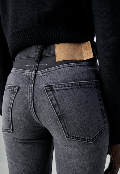 Skinny grey jeans with a textured black waistband and a brown leather patch at the back, featuring standard back pockets and visible stitching.