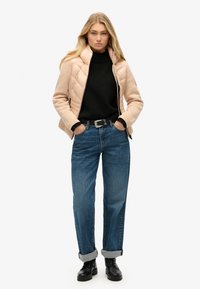 Beżowa kurtka pikowana na czarnym golfie, zestawiona z jasnoniebieskimi dżinsami z podwiniętymi rękawami oraz czarnymi sznurowanymi butami. Prosty i funkcjonalny design.