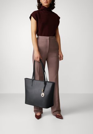 Bolso tote de cuero negro con un diseño estructurado, dos asas largas y un charm de logo dorado. Textura suave y acentos minimalistas.