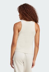 Top sin mangas de color beige claro, ajustado, con escote redondo y sisas amplias, fabricado en una tela suave y elástica. Combinado con pantalones a juego.