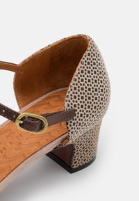 Sandale à talon avec une tige texturée beige et noire à motifs, des brides en cuir marron et une semelle intérieure rembourrée beige. Agrément ée d'une boucle dorée.