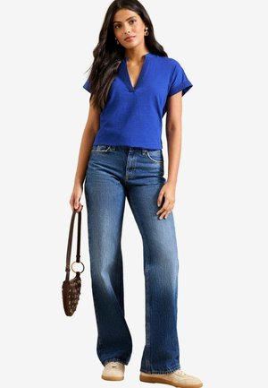 Blue short-sleeve top with a V-neck, paired with light blue wide-leg jeans. Brown handbag with a textured pattern. Casual footwear.