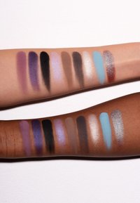 Due braccia che mostrano campioni di ombretto: varie tonalità tra cui viola, nero, blu e neutri con finiture lucide e opache.