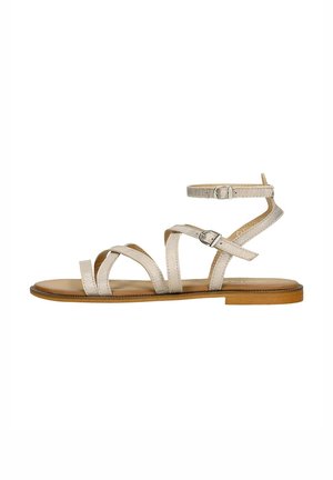 Strappy sandal with a flat sole, featuring metallic beige straps and an adjustable ankle buckle. Natural wood-tone platform.