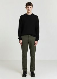 Maglione nero a coste, pantaloni verde oliva, scarpe nere, design semplice, materiale texturizzato, vestibilità comoda, in piedi contro uno sfondo neutro.