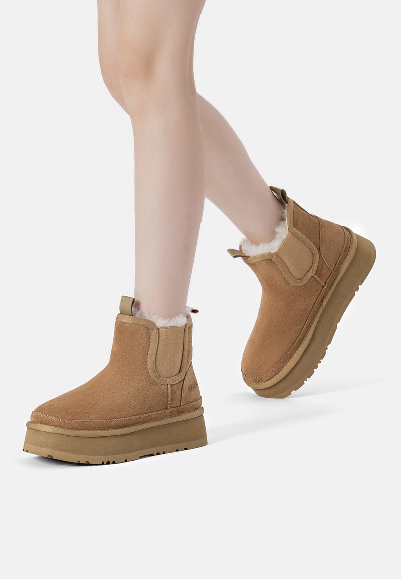 Sandfarbene Wildleder-Stiefeletten mit weicher Kunstfell-Fütterung, elastischen seitlichen Einsätzen und strukturiertem Gummisohle, die ein robustes, abgerundetes Design präsentieren.