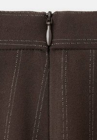 Tessuto marrone con finitura testurizzata, caratterizzato da una cerniera centrale e sottili righe bianche verticali come dettaglio. Presenta un cursore della cerniera scuro come accento.