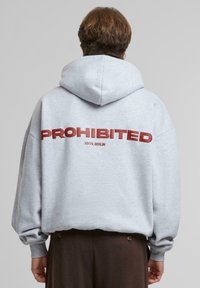 Un sweat à capuche gris avec un grand texte rouge "INTERDIT" au dos, accompagné de "10119, BERLIN." Coupe ample et tissu doux et texturé avec une capuche.
