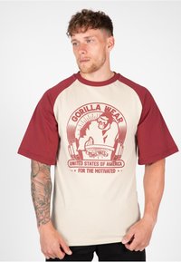 T-shirt met korte mouwen met een beige lichaam en maroon raglanmouwen. Heeft een grafische print van een gorilla en rode tekst. Zachte stoftextuur.