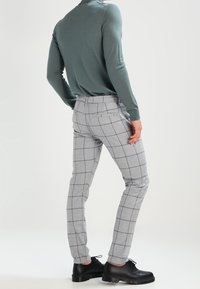 Szare spodnie w kratę o dopasowanym kroju, z czarnymi liniami. Połączone z zieloną bluzką z długim rękawem i czarnymi butami. Gładka faktura.