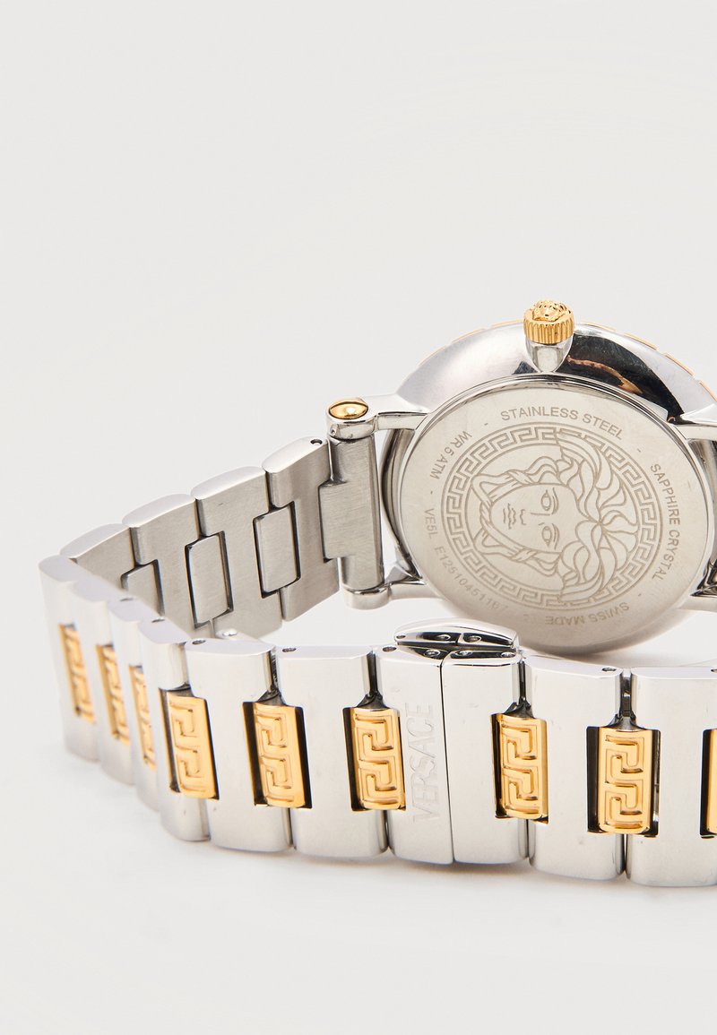 Bracelet de montre en métal argenté et doré avec tête de Méduse gravée sur le dos en acier inoxydable et logo Versace sur la boucle.