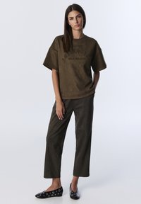 Olijfgroene oversized t-shirt met een textuurafwerking en reliëflettering; gecombineerd met op maat gemaakte donkergroene broek en gestipte zwarte ballerina's.