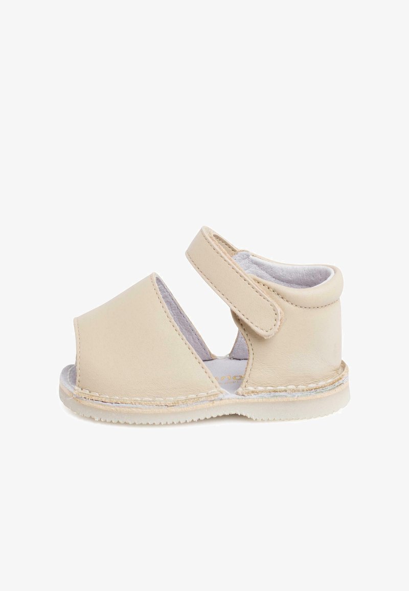 Sandale en cuir beige avec un talon fermé et une pointe ouverte, dotée d'une sangle réglable, d'une texture lisse et de détails cousus le long de la semelle.