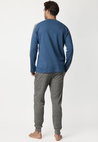 Camisa azul de manga larga con detalles en gris, combinada con pantalones de chándal grises. El material parece suave; ajuste casual con puños y cintura acanalados.