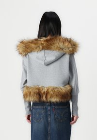 Κοντό γκρι φούτερ με καφέ ψεύτικη γούνα στην κουκούλα και στο κάτω μέρος, συνδυασμένο με τζιν φούστα που έχει πίσω τσέπες.