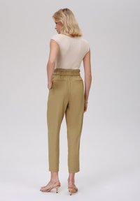 Beige ribbestrikket topp kombinert med høy midje, olivengrønne bukser som har elastisk midje og sidelommer. Beige sandaler med stropper.