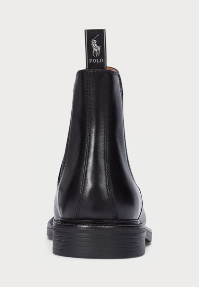 Black leather chelsea boot featuring a smooth finish, elastic side panels, and a branded pull tab at the back. Flat rubber sole.