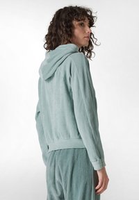 Sudadera de corduroy verde claro con un corte relajado, textura acanalada y capucha; presenta mangas acampanadas y un dobladillo corto.
