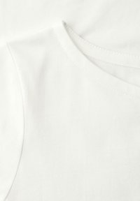 Primo piano di tessuto di cotone bianco semplice con cuciture visibili che formano parte di una scollatura arrotondata e dell'area della spalla.